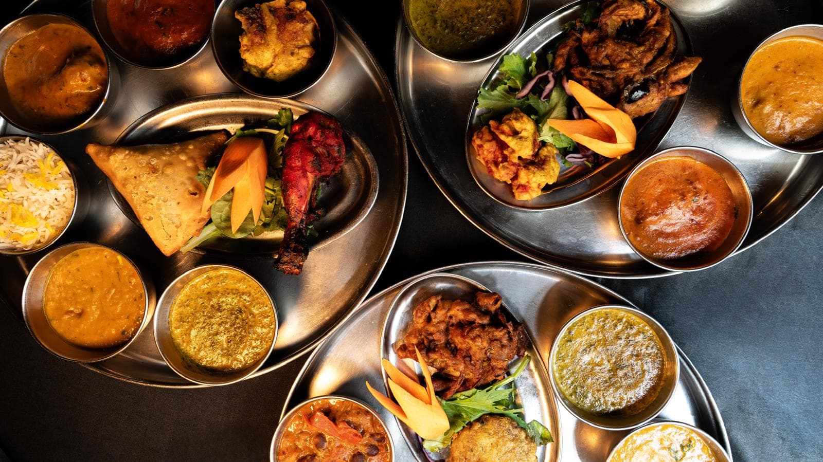 Trois thalis complets vus du dessus : currys, dal, riz safrané et tandoori