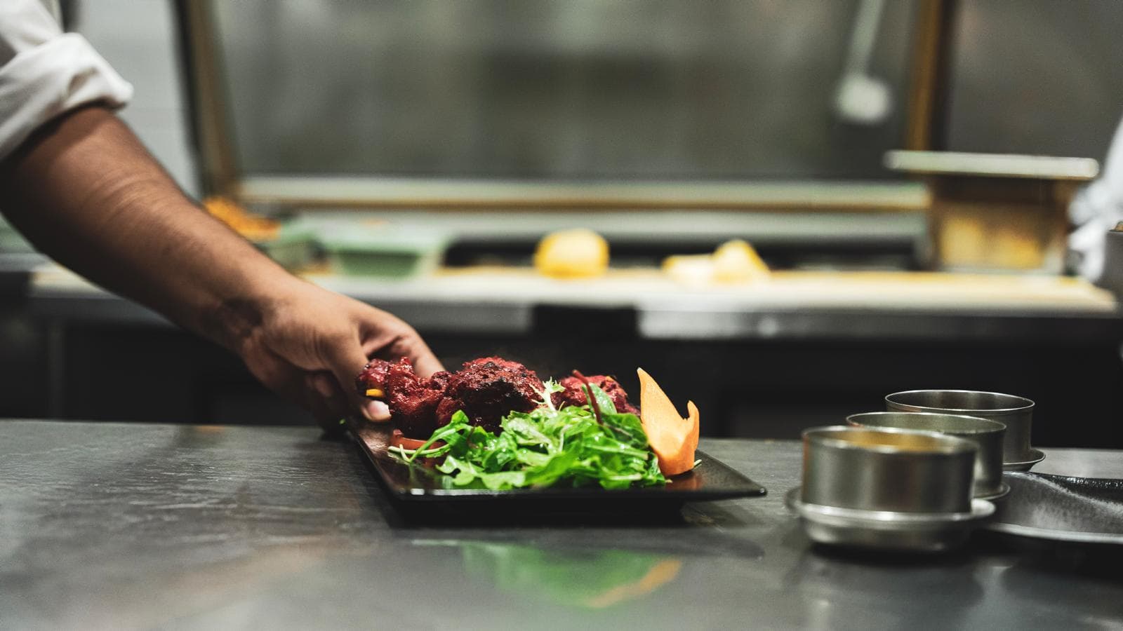 Main du chef déposant une assiette de tandoori au passe de la cuisine