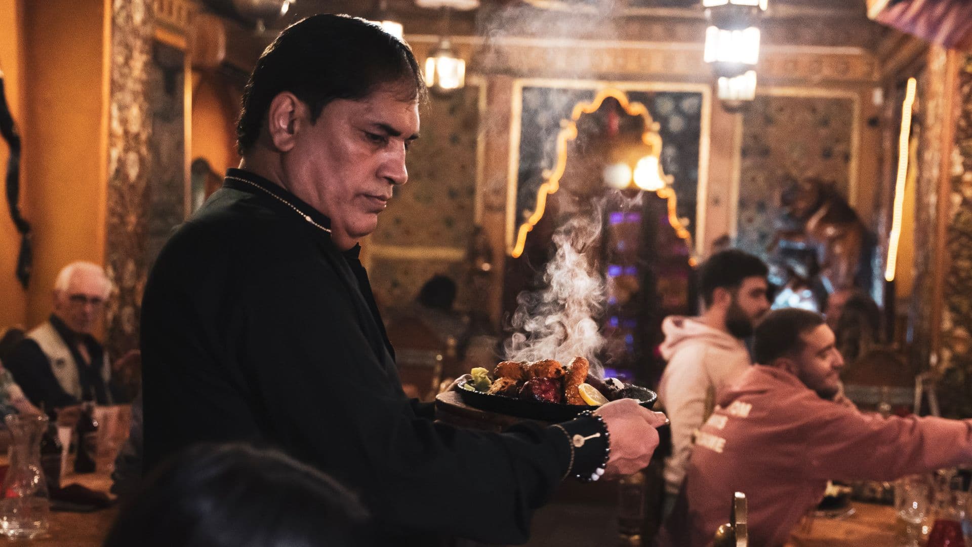 Serveur portant un sizzler fumant entre les tables de la salle ornée d'O'Pakistan